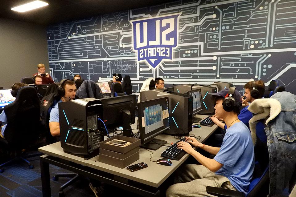 Esports players at two tables with headphones and CPUs with the eports logo in the background